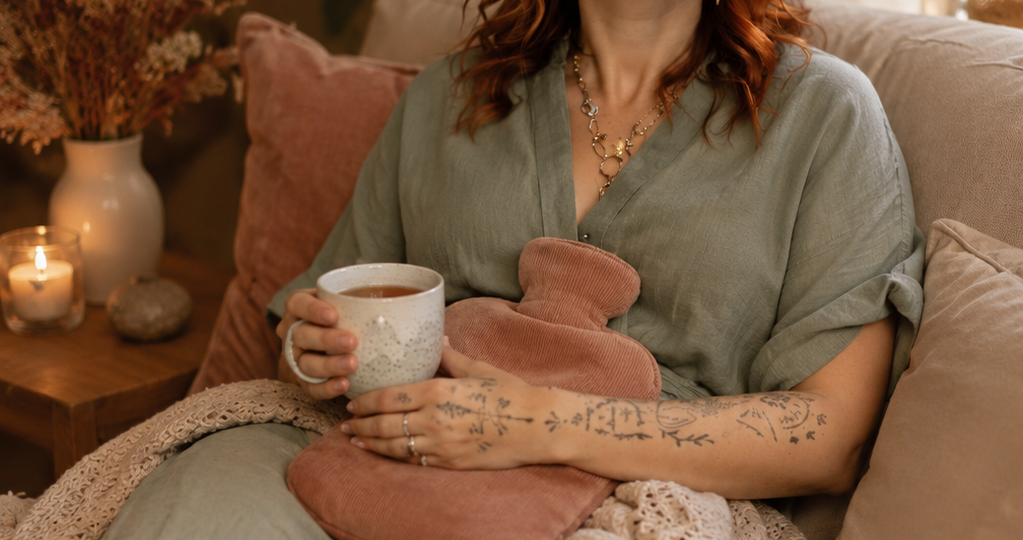 Femme se reposant après un rituel de soin pour l'endométriose aevc une bouillotte sur le ventre et une tisane, dans une ambiance cocooning